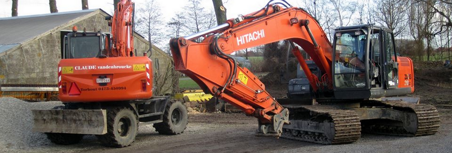Twee oranje graafmachines van Claude Vandenbroucke naast elkaar op een grindterrein voor een loods
