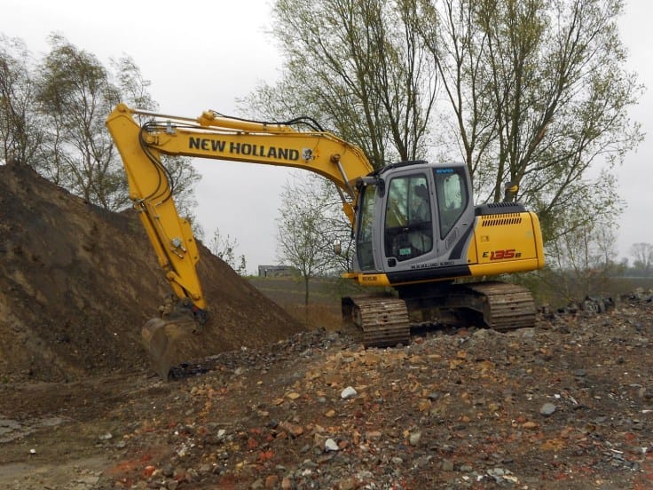 Gele NEW HOLLAND rupskraan bovenop een grote aardeberg die grond afgraaft