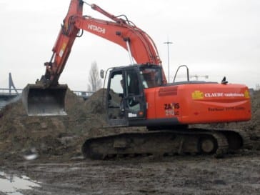 Oranje Hitachi rupskraan die een grote zandberg afgraaft op een modderig terrein