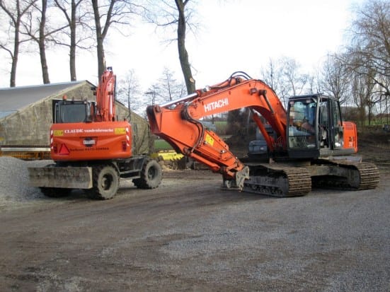 Oranje mobiele kraan en grotere Hitachi rupskraan naast elkaar voor een loods