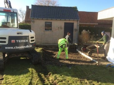 Grijze TEREX kraan en arbeider die met kruiwagen aardewerk verzet bij een woning