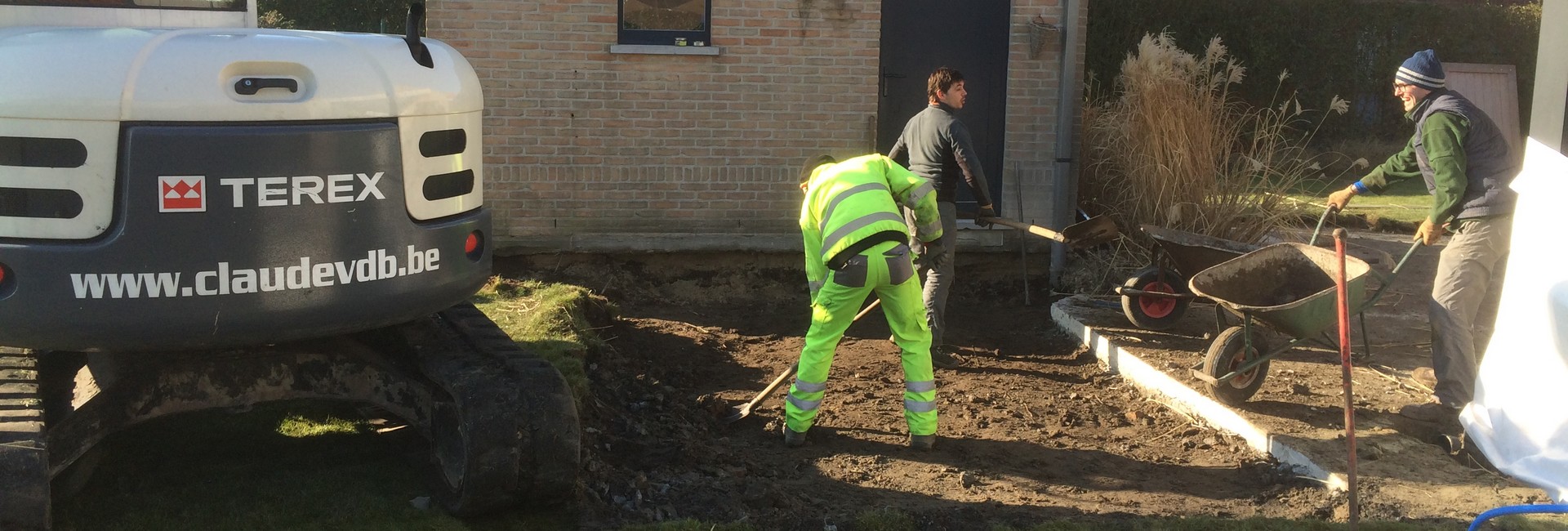 Grijze TEREX rupskraan en arbeiders die een tuinoprit aanleggen bij een woning